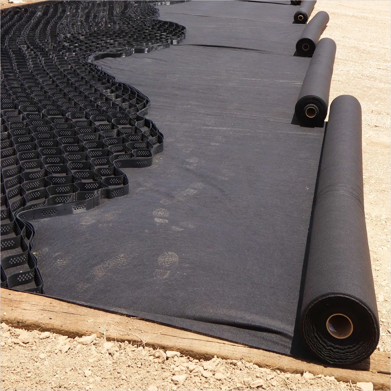 Geotextil negro extendido bajo geocelda, con rollos listos para instalar — MF Design